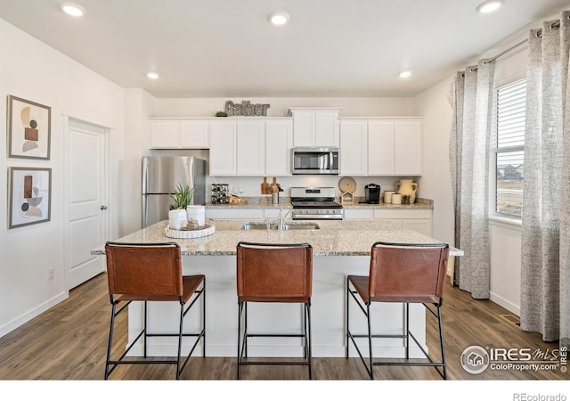 kitchen with dark hardwood / wood-style flooring, a kitchen island with sink, white cabinetry, and stainless steel appliances