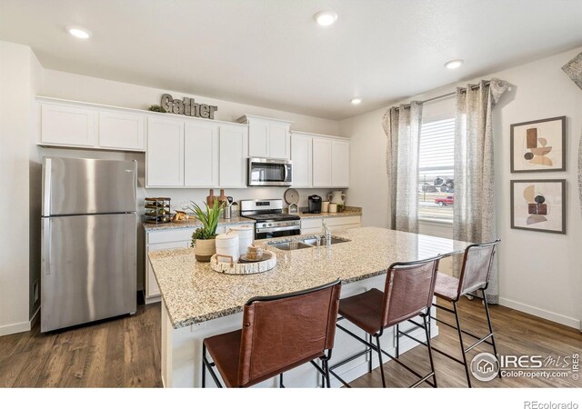 kitchen with a breakfast bar, white cabinets, stainless steel appliances, and a kitchen island with sink