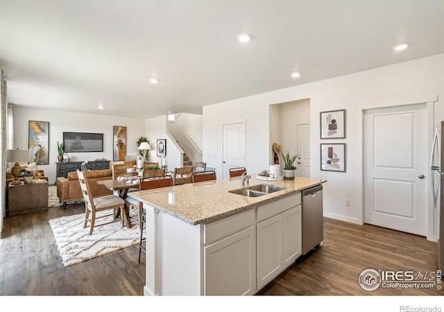 kitchen with dishwasher, sink, white cabinets, light stone countertops, and a center island with sink