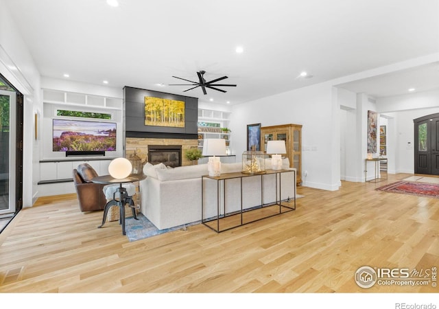 living room featuring ceiling fan, built in features, light hardwood / wood-style flooring, and a stone fireplace