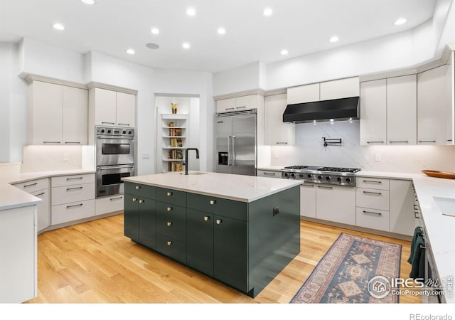 kitchen with appliances with stainless steel finishes, tasteful backsplash, a kitchen island with sink, wall chimney range hood, and white cabinets