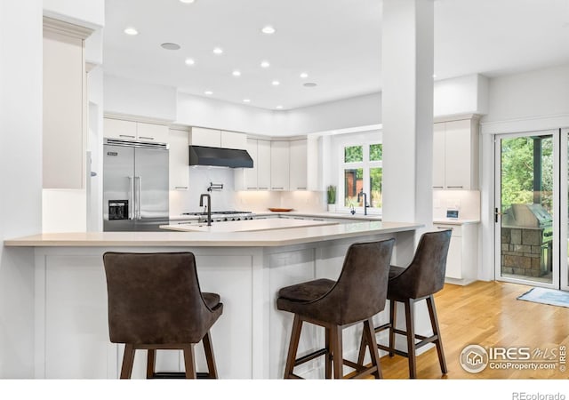 kitchen featuring kitchen peninsula, white cabinetry, a breakfast bar, and stainless steel built in refrigerator