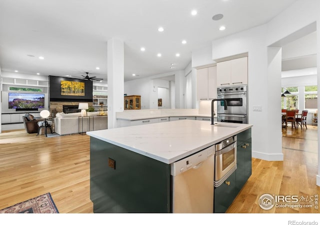 kitchen featuring dishwasher, white cabinetry, light hardwood / wood-style flooring, light stone counters, and a center island with sink