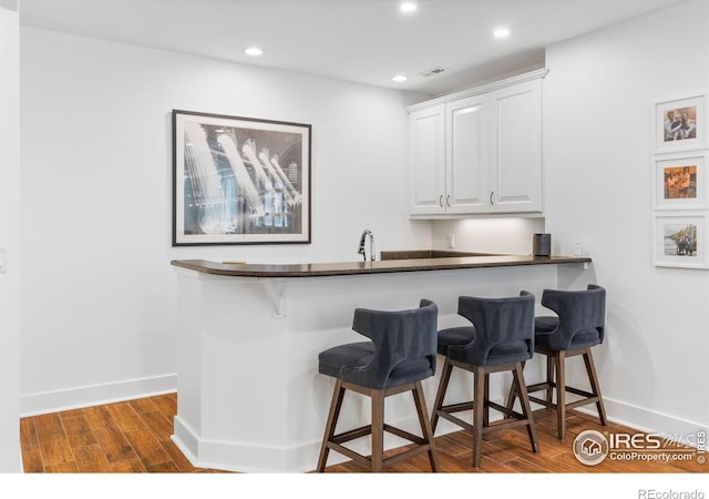 kitchen featuring a kitchen breakfast bar, white cabinets, dark hardwood / wood-style flooring, and kitchen peninsula