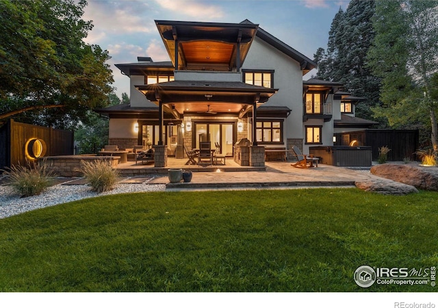 back house at dusk with a patio and a lawn