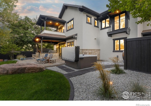 back house at dusk with a balcony, a patio area, and a hot tub