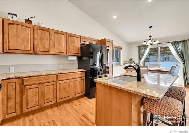 kitchen featuring lofted ceiling, black refrigerator, sink, hanging light fixtures, and light stone counters