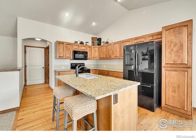 kitchen featuring sink, a kitchen bar, a center island with sink, black appliances, and lofted ceiling