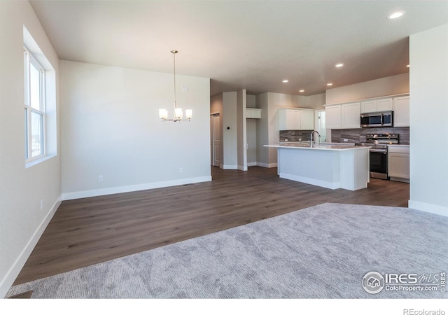 kitchen featuring appliances with stainless steel finishes, decorative light fixtures, tasteful backsplash, white cabinets, and a kitchen island with sink