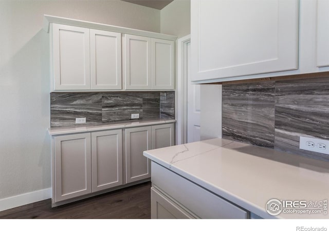 kitchen with backsplash, dark wood-type flooring, light stone counters, and white cabinets