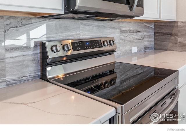 kitchen with backsplash, stainless steel appliances, light stone countertops, and white cabinets