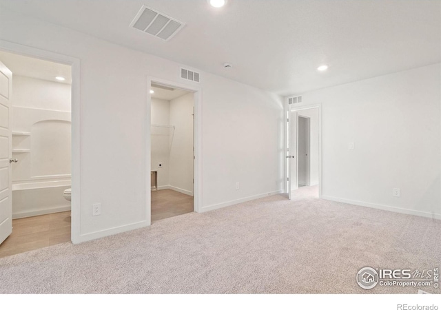 unfurnished bedroom featuring light carpet, ensuite bath, and a walk in closet