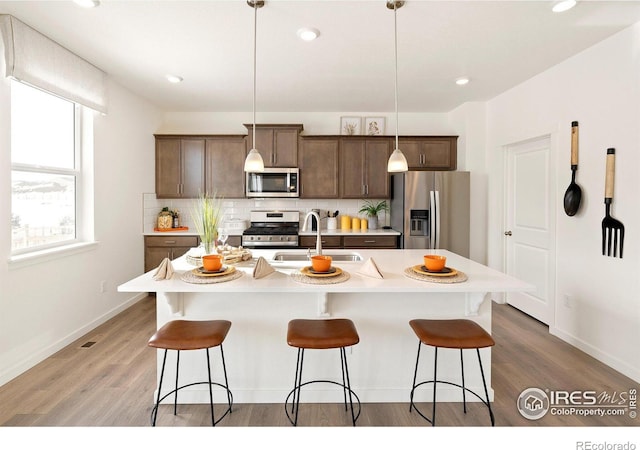 kitchen with pendant lighting, sink, tasteful backsplash, a center island with sink, and stainless steel appliances