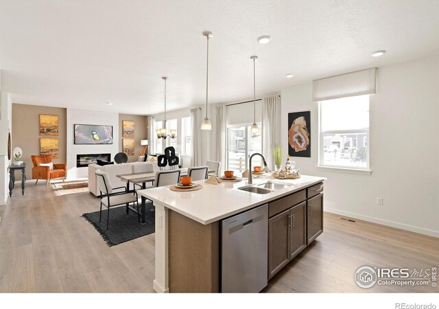 kitchen with a fireplace, sink, light wood-type flooring, stainless steel dishwasher, and a center island with sink