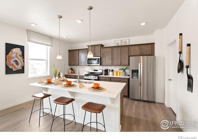 kitchen with a kitchen island with sink, dark hardwood / wood-style floors, hanging light fixtures, and appliances with stainless steel finishes