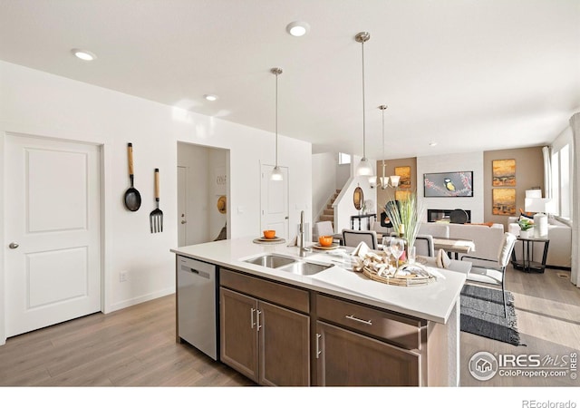 kitchen with dishwasher, sink, decorative light fixtures, a fireplace, and a kitchen island with sink