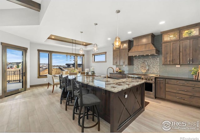 kitchen with hanging light fixtures, a spacious island, custom range hood, light stone counters, and double oven range