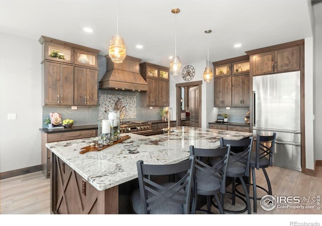 kitchen with a large island, sink, premium range hood, decorative light fixtures, and high end fridge