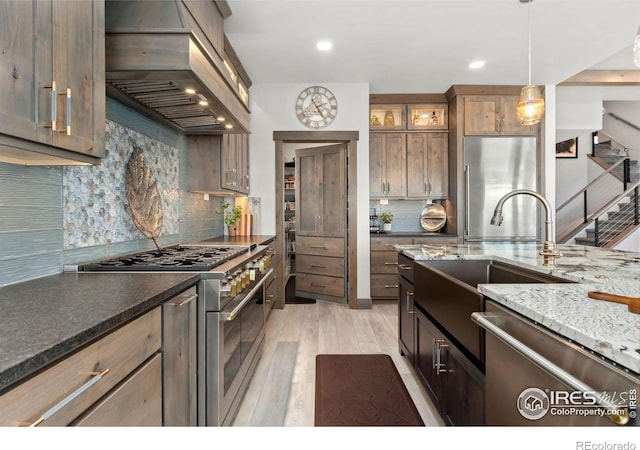 kitchen featuring premium appliances, hanging light fixtures, backsplash, light wood-type flooring, and island range hood