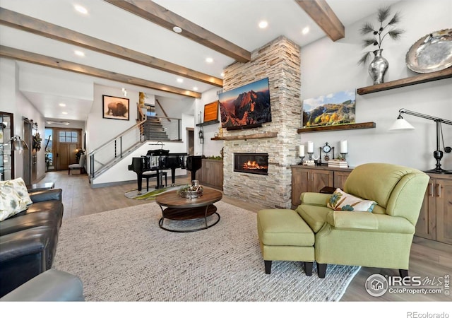 living room featuring a stone fireplace, beamed ceiling, and light hardwood / wood-style floors