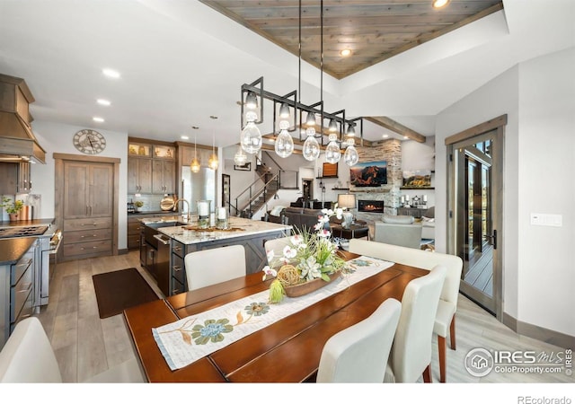 dining room featuring a raised ceiling, sink, wood ceiling, a fireplace, and light hardwood / wood-style floors