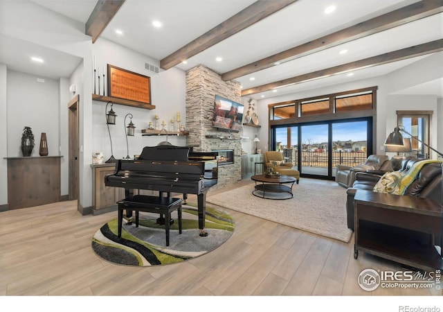 living room with beam ceiling, a stone fireplace, and light wood-type flooring