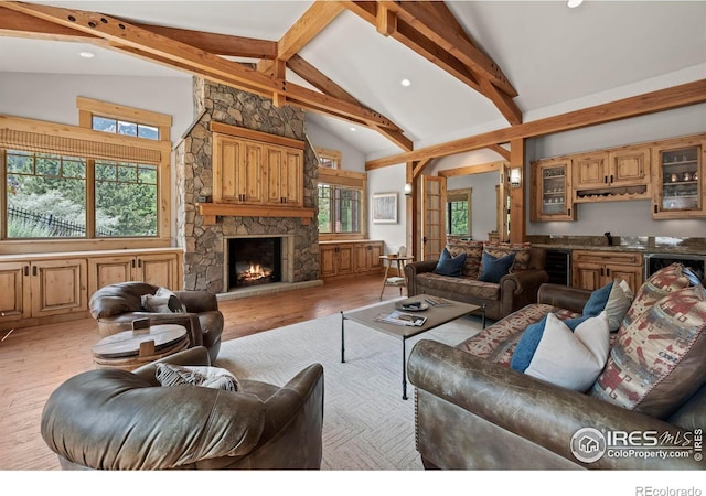 living room featuring indoor bar, a stone fireplace, beamed ceiling, light hardwood / wood-style floors, and high vaulted ceiling