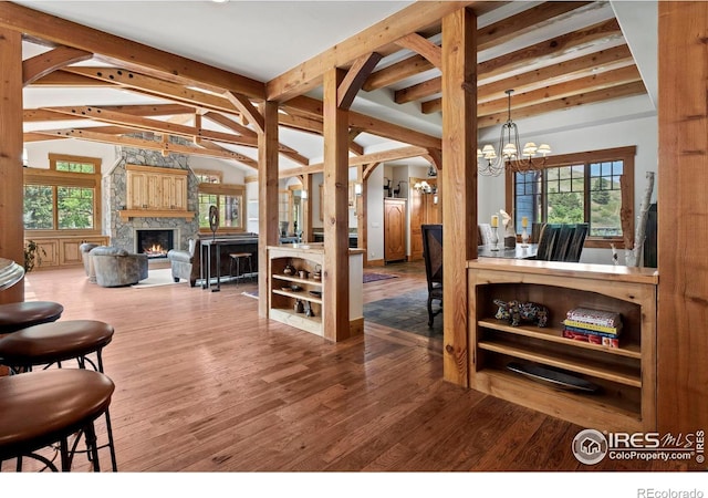 interior space featuring hardwood / wood-style flooring, a stone fireplace, an inviting chandelier, and lofted ceiling with beams