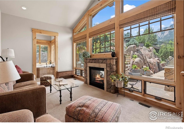 carpeted living room with a mountain view, a stone fireplace, and vaulted ceiling