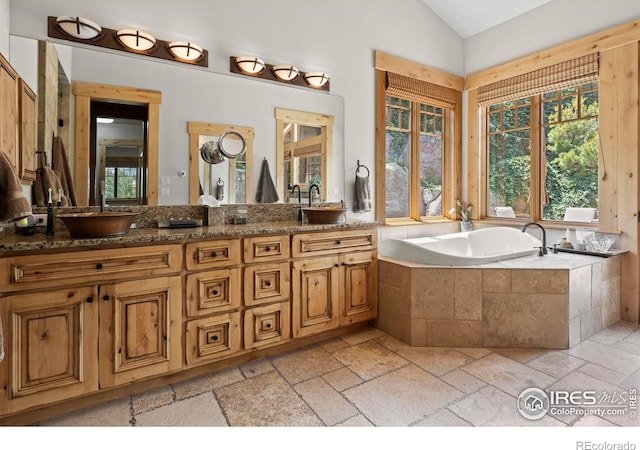 bathroom featuring vaulted ceiling, a relaxing tiled tub, and vanity