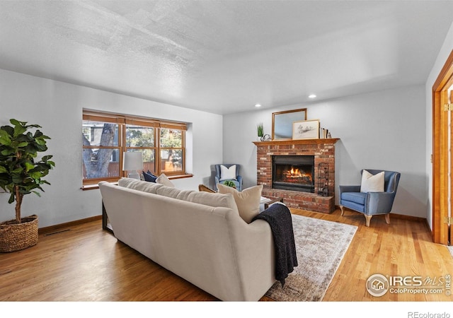 living room featuring a brick fireplace, light hardwood / wood-style flooring, and a textured ceiling