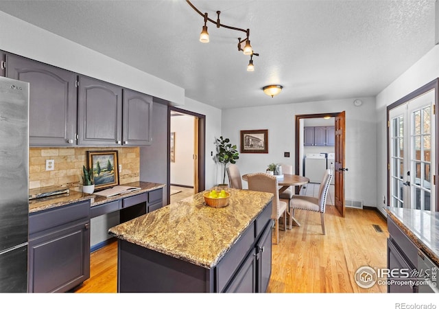 kitchen with light stone counters, stainless steel refrigerator, a kitchen island, washing machine and dryer, and decorative backsplash