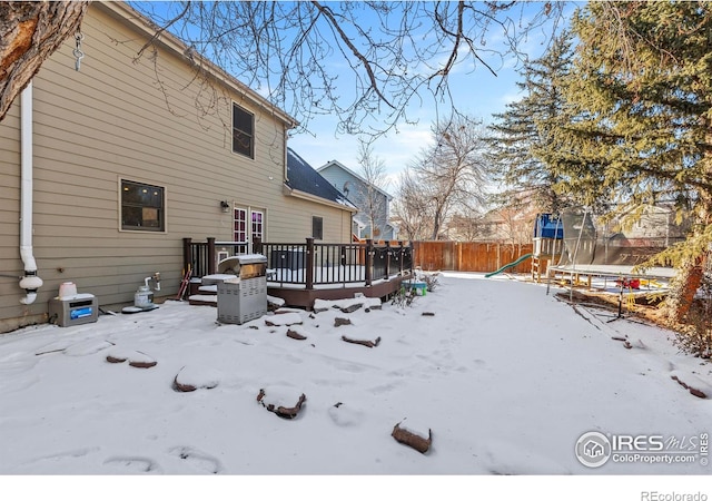 snow covered house with a trampoline, a playground, and a deck