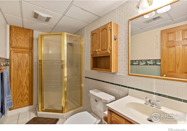 bathroom featuring a shower with shower door, tile walls, tile patterned flooring, vanity, and toilet