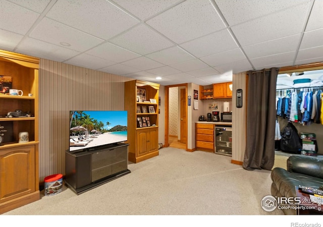 living room featuring indoor bar, light carpet, beverage cooler, and a drop ceiling