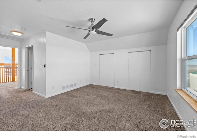 unfurnished bedroom featuring multiple closets, ceiling fan, carpet, and vaulted ceiling