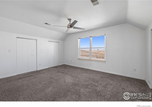 unfurnished bedroom with dark colored carpet, vaulted ceiling, ceiling fan, and multiple closets