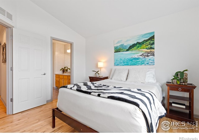 bedroom featuring light hardwood / wood-style floors, ensuite bath, and lofted ceiling