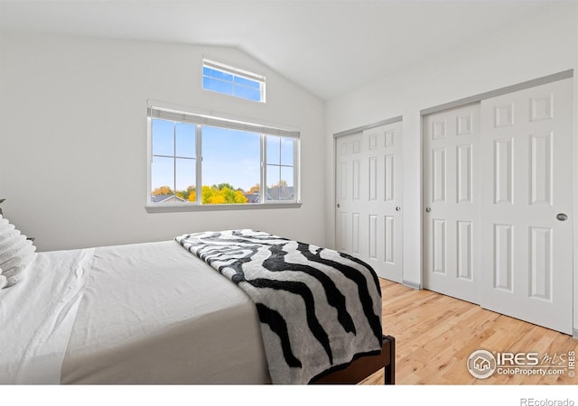 bedroom featuring two closets, wood-type flooring, and lofted ceiling