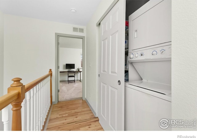 laundry room with stacked washer / drying machine and light hardwood / wood-style flooring