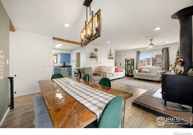 dining space with light hardwood / wood-style floors, a wood stove, beam ceiling, and ceiling fan