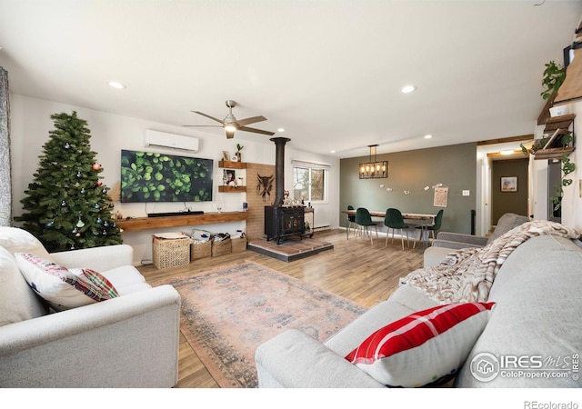 living room featuring ceiling fan, light hardwood / wood-style flooring, an AC wall unit, and a wood stove