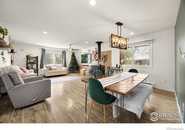 dining room featuring a wood stove, ceiling fan with notable chandelier, light hardwood / wood-style flooring, and baseboard heating