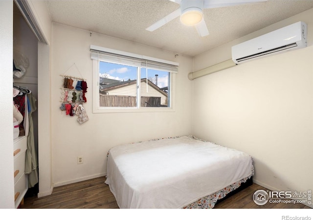 bedroom with a textured ceiling, a wall mounted air conditioner, dark hardwood / wood-style floors, and ceiling fan