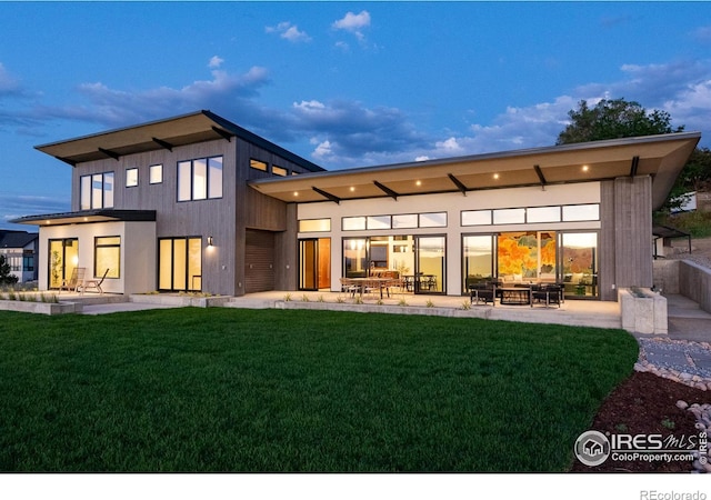 back house at dusk with a patio area and a lawn