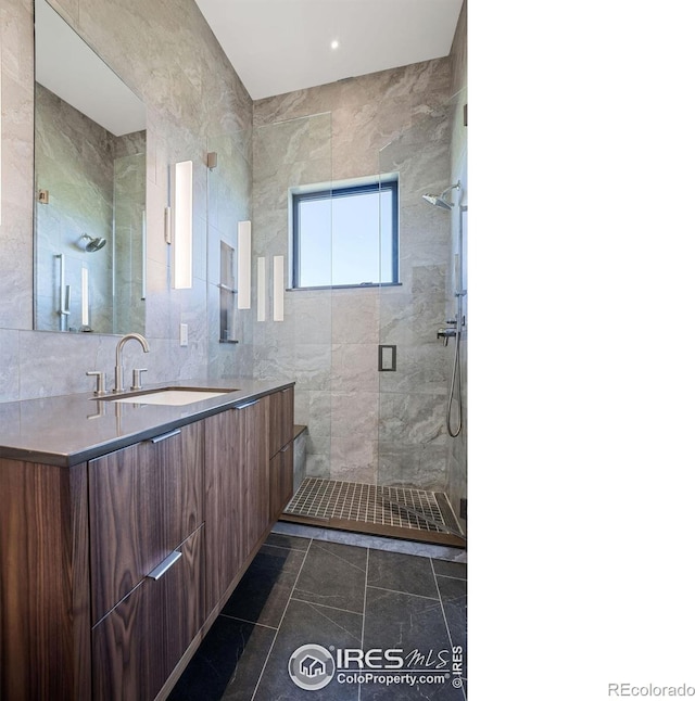 bathroom with vanity, tiled shower, and tile walls