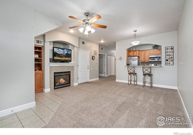 unfurnished living room with ceiling fan, a tile fireplace, light tile patterned floors, and a textured ceiling