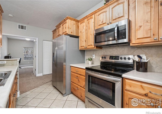 kitchen with a textured ceiling, stainless steel appliances, sink, backsplash, and light tile patterned floors