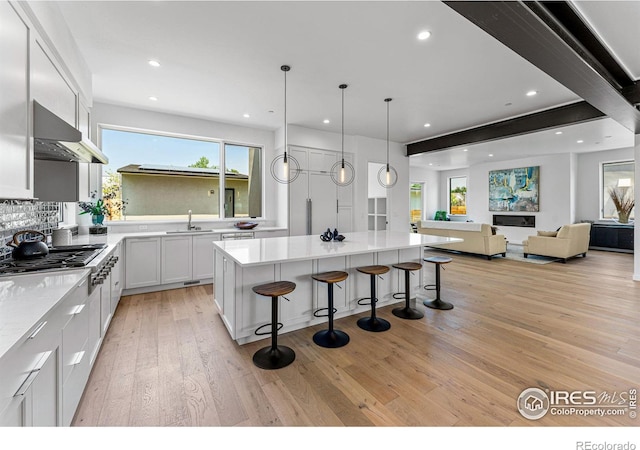 kitchen with exhaust hood, a kitchen bar, light hardwood / wood-style floors, white cabinetry, and sink