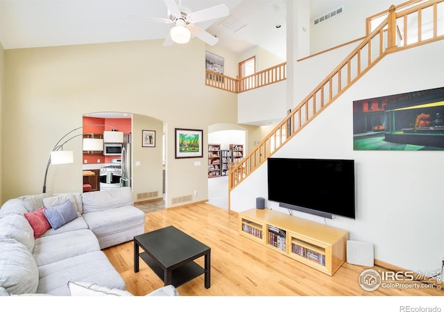 living room featuring ceiling fan, hardwood / wood-style floors, and a towering ceiling